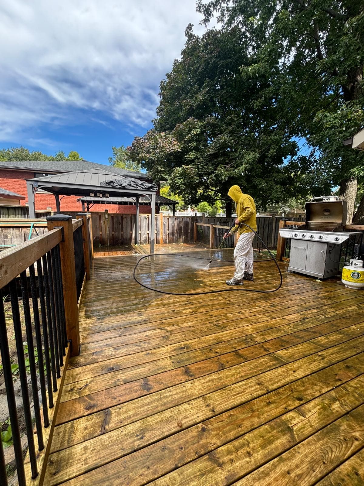 Painter pressure washing a weathered backyard deck before refinishing